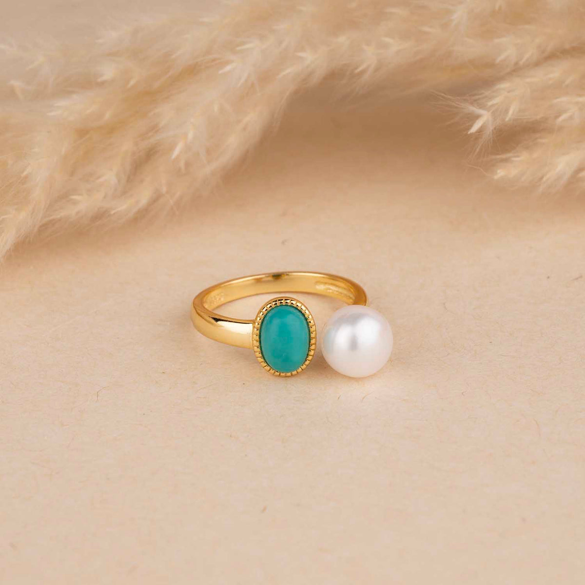 Gold ring with turquoise gemstone and pearl on a beige background