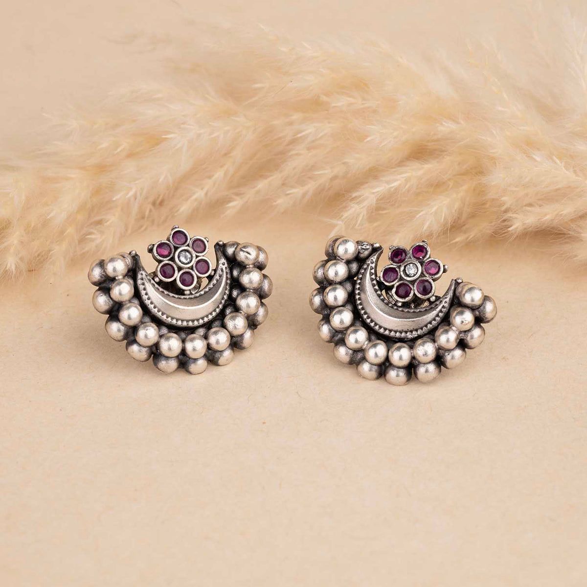Pair of silver earrings with pearl-like beads and purple gemstones on a beige fur background
