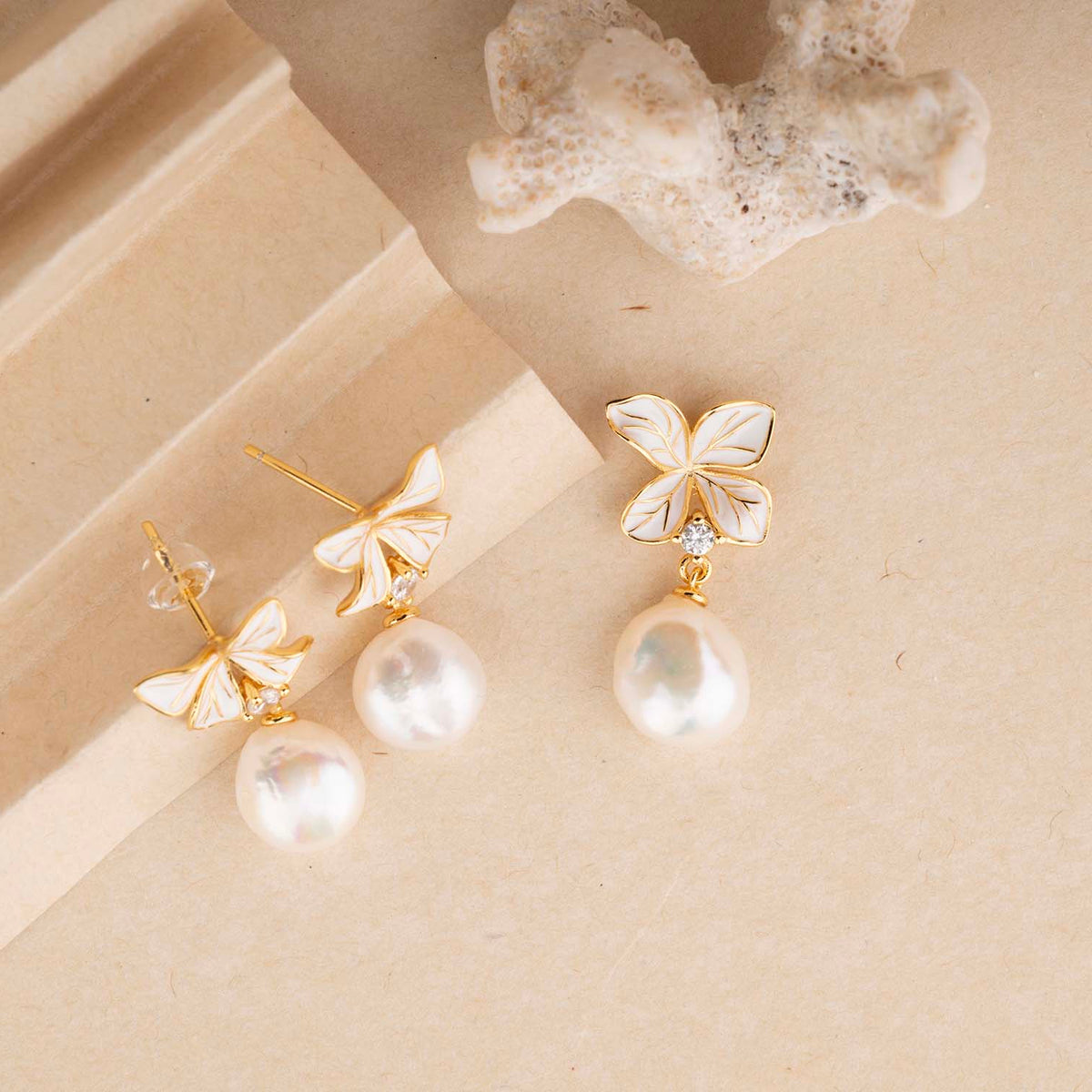 Pair of butterfly-shaped earrings with pearl drops on a beige surface.